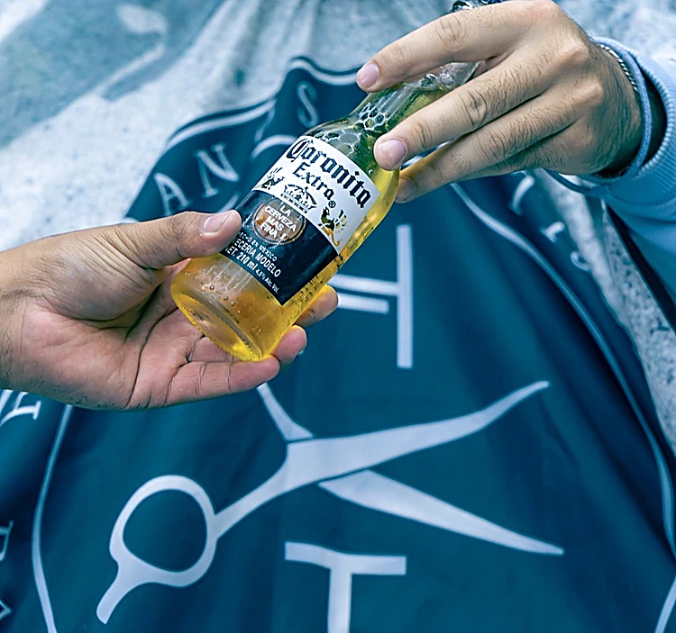 Cerveza destapándose sobre la capa con el logo de Hermanos de Tijera