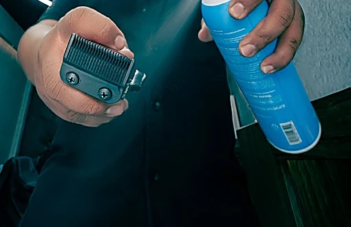 Manos rociando desinfectante sobre la cuchilla de la máquina antes del servicio