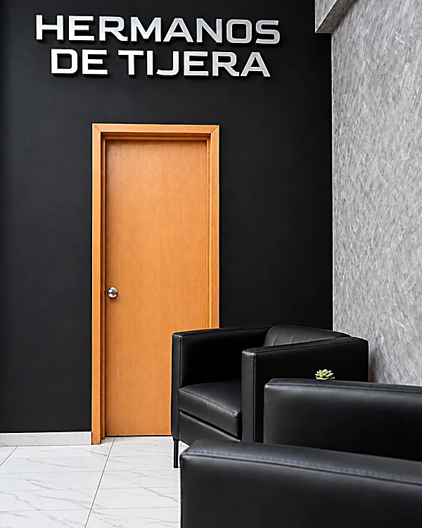Muro negro con las letras Hermanos de Tijera, puerta de madera y sillones de piel