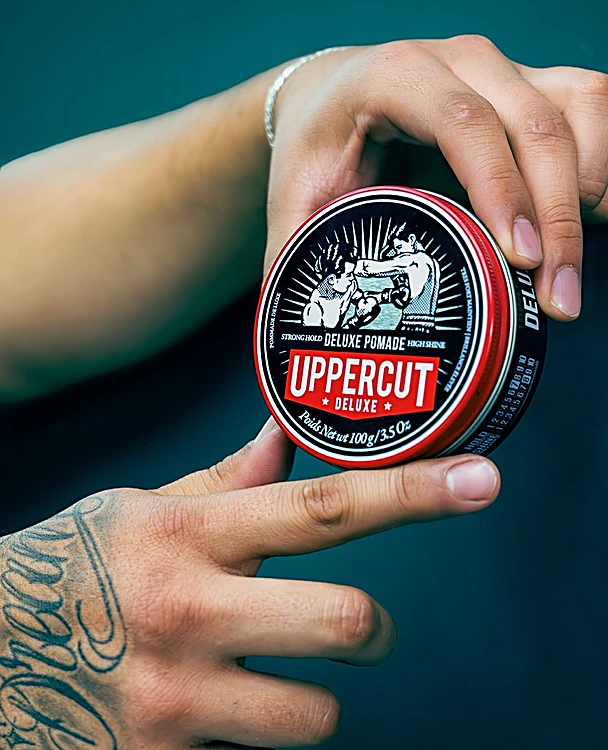 Lata roja de pomada Uppercut Deluxe en manos tatuadas
