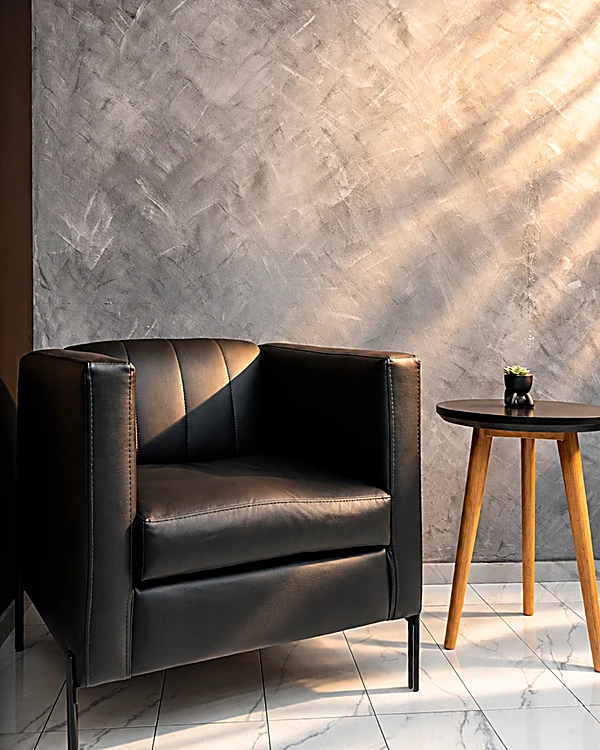 Sala de espera con sillón de piel negro, mesita de madera y muro de concreto pulido
