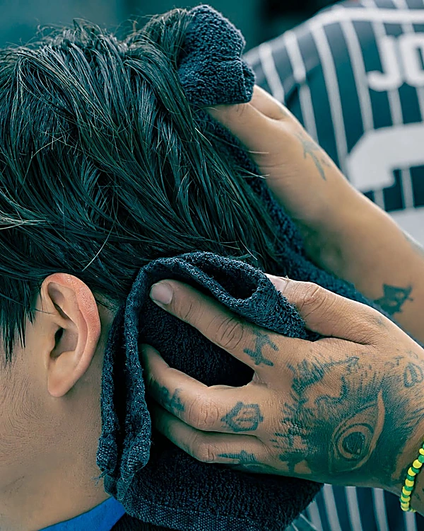 Manos tatuadas secando el cabello con toalla después del lavado